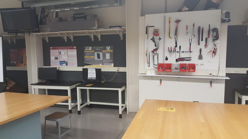 The lab with few Tables, monitors, a TV screen and a white pegboard with tools mounted on it.