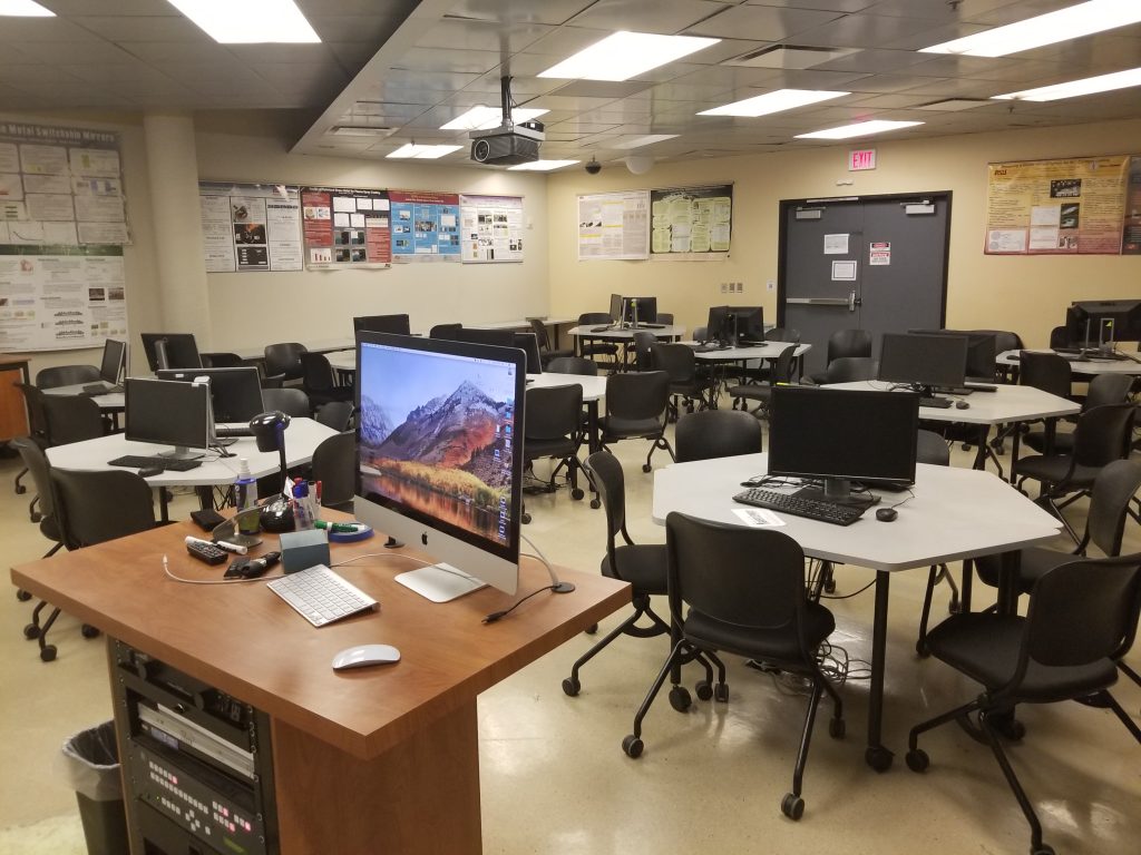 A lab that has several round tables with monitors and an instrutor station