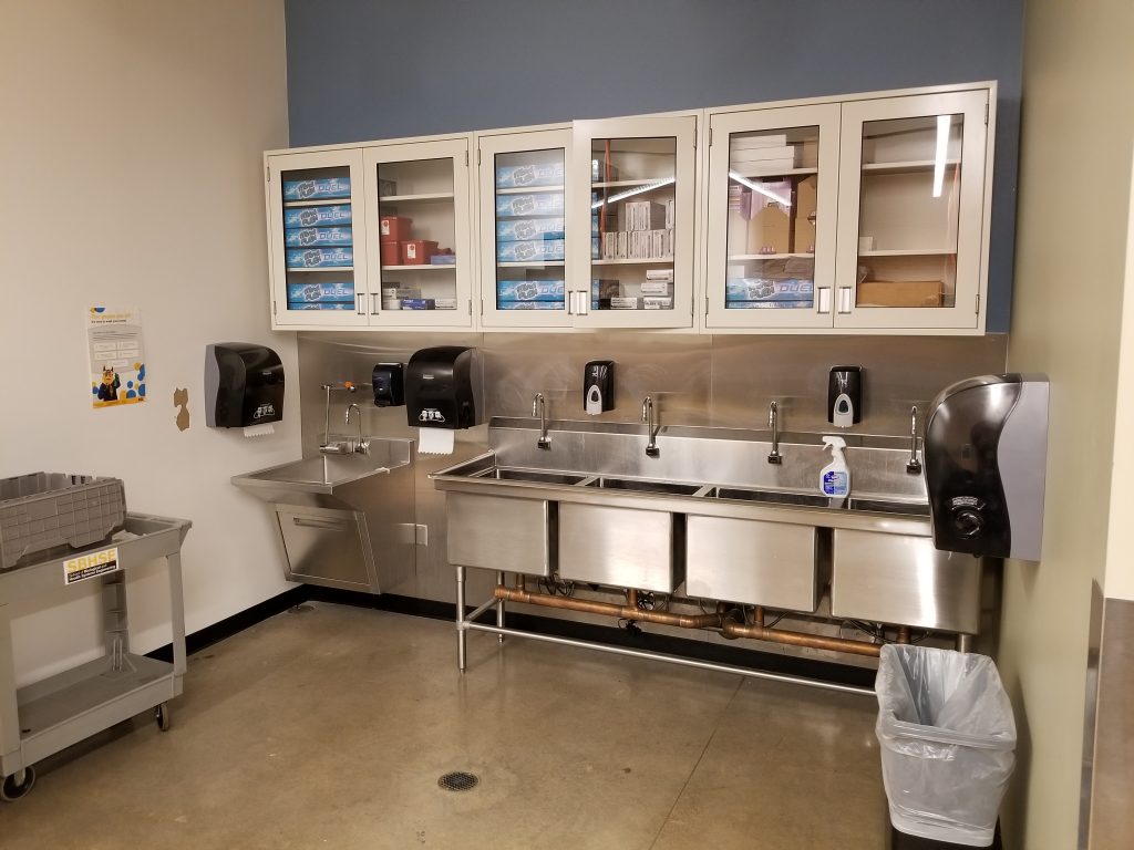 A room with sinks, hand wash dispensers, and other cleaning supplies stored in cabinets.