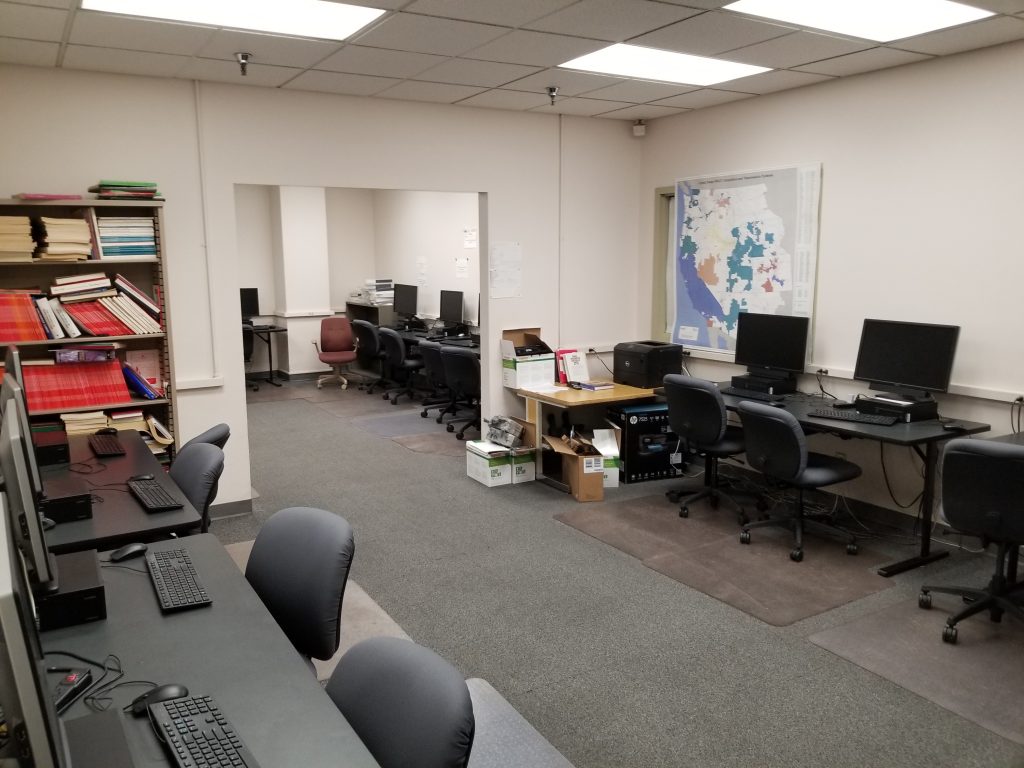 Instructional lab with two rooms and several desks, computers, printers, and chairs along the walls. 