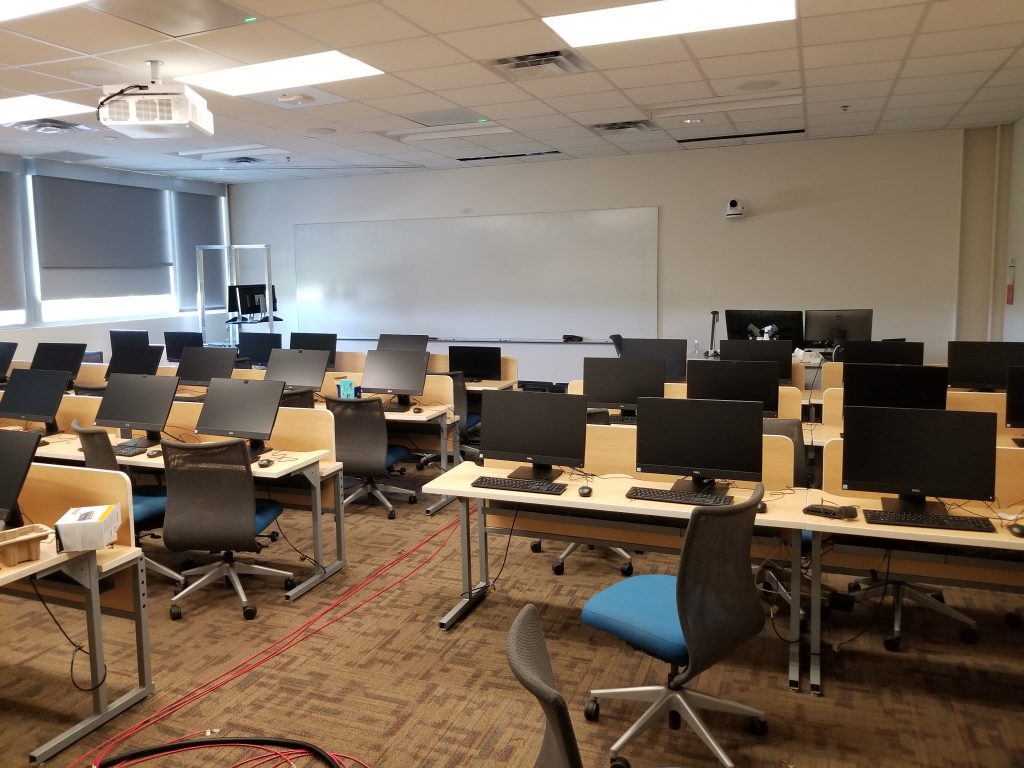 Photograph of a classroom (PRLTA 201). Shown are many desks, chairs and computers (the screens of which are visible). On the far wall is a large whiteboard. In front of the whiteboard the instructor's work station is located. 