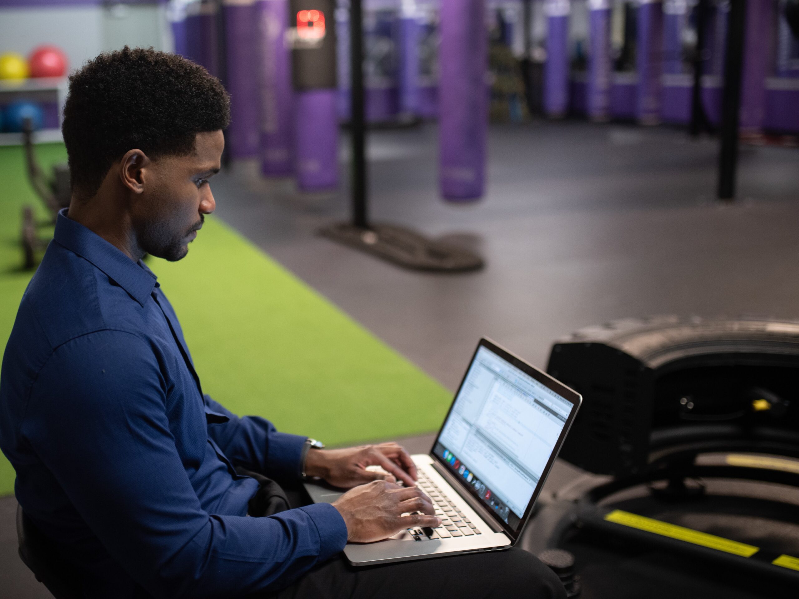 Man sitting in gym using a laptop.